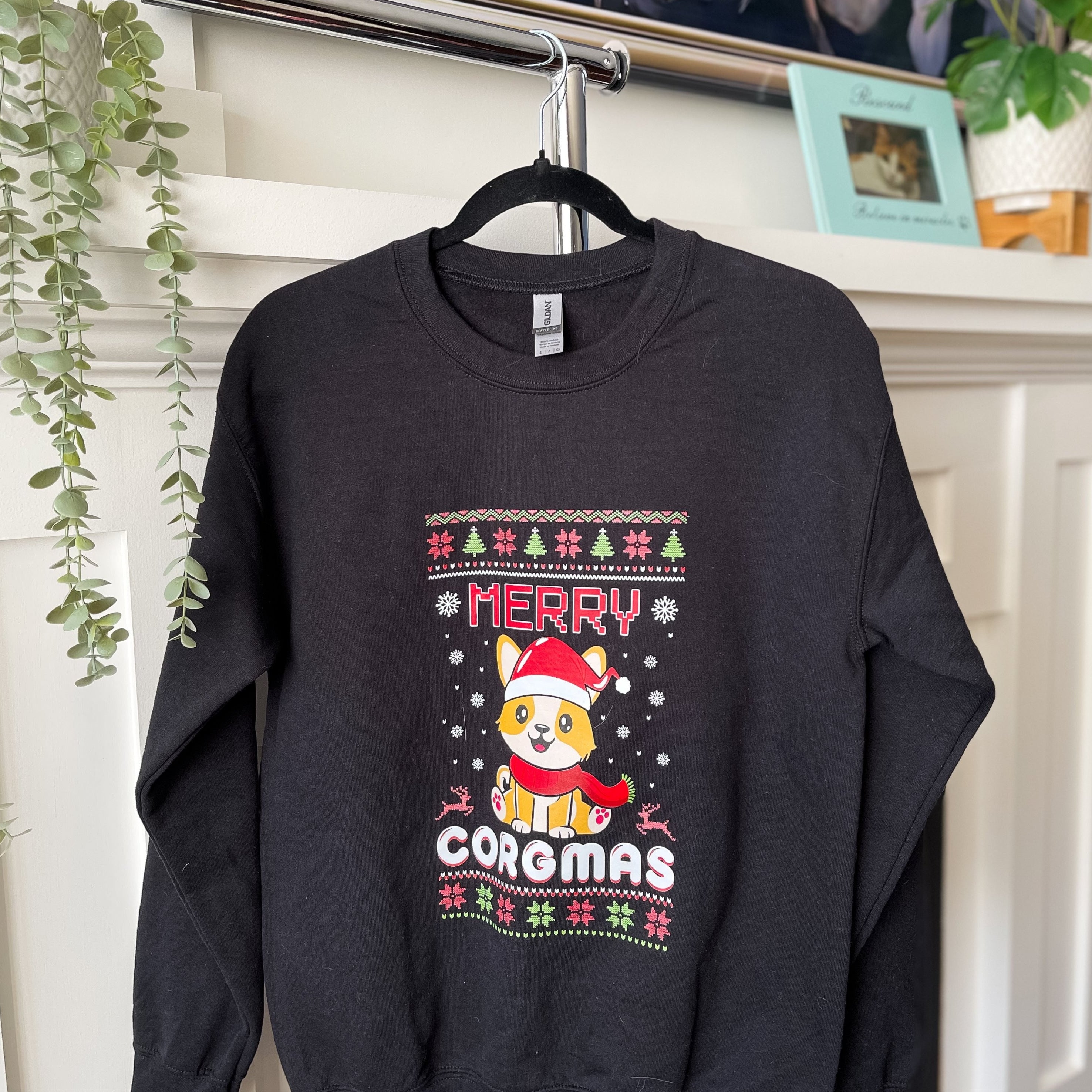 A black sweater with a festive design featuring a corgi, Christmas trees, and the text 'Merry CORGMAS'.