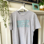 Gray t-shirt with humorous text on a hanger against a neutral background