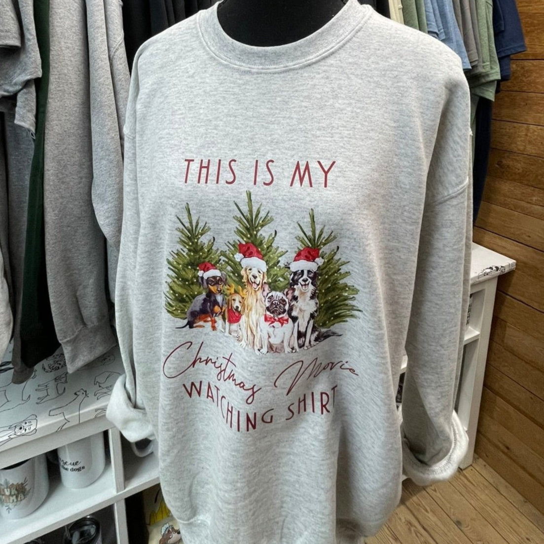 Gray sweater with a Christmas themed design featuring dogs in Santa hats and trees, and the text 'This is my Christmas watching shirt'.
