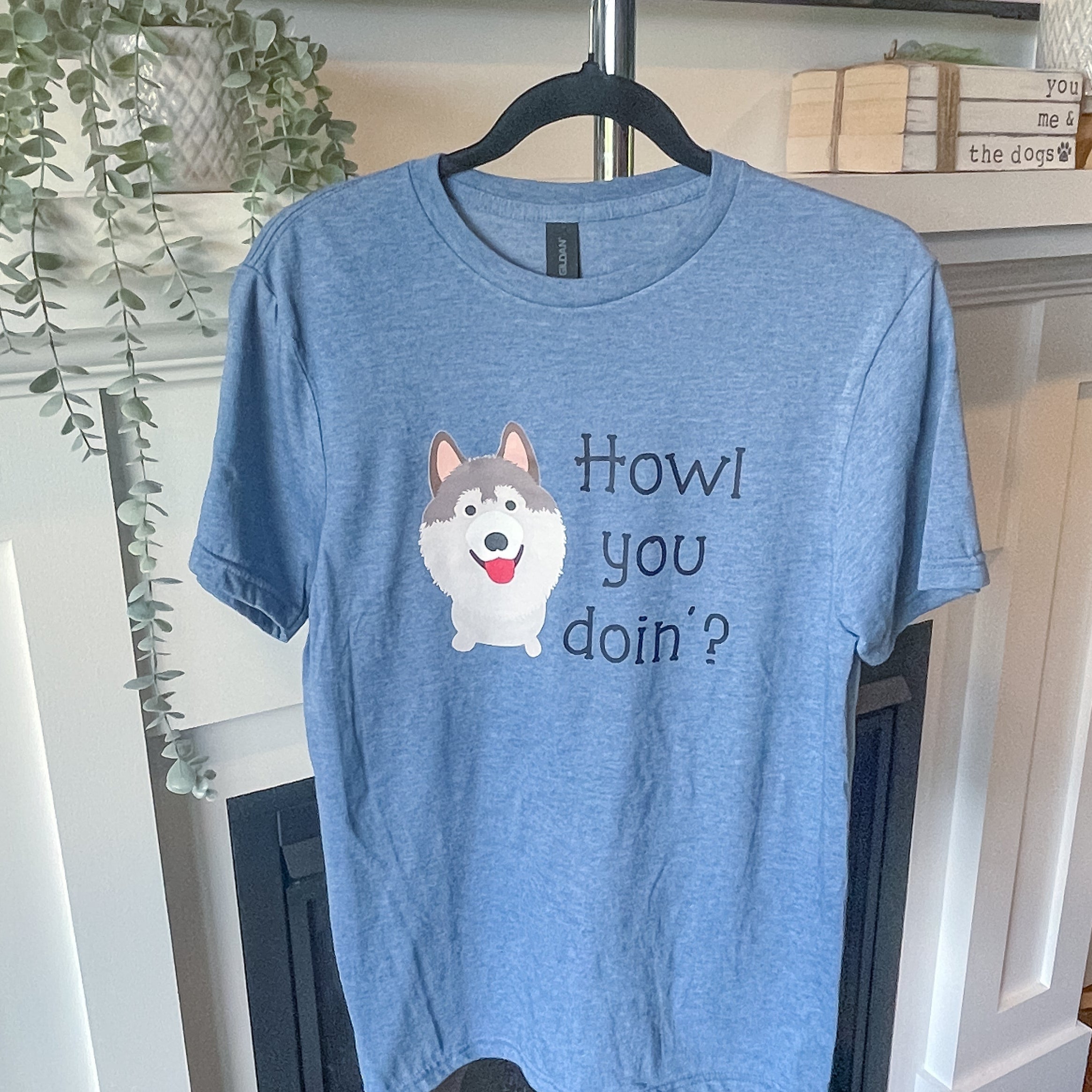 Blue t-shirt with a dog graphic and text on a hanger in a room.