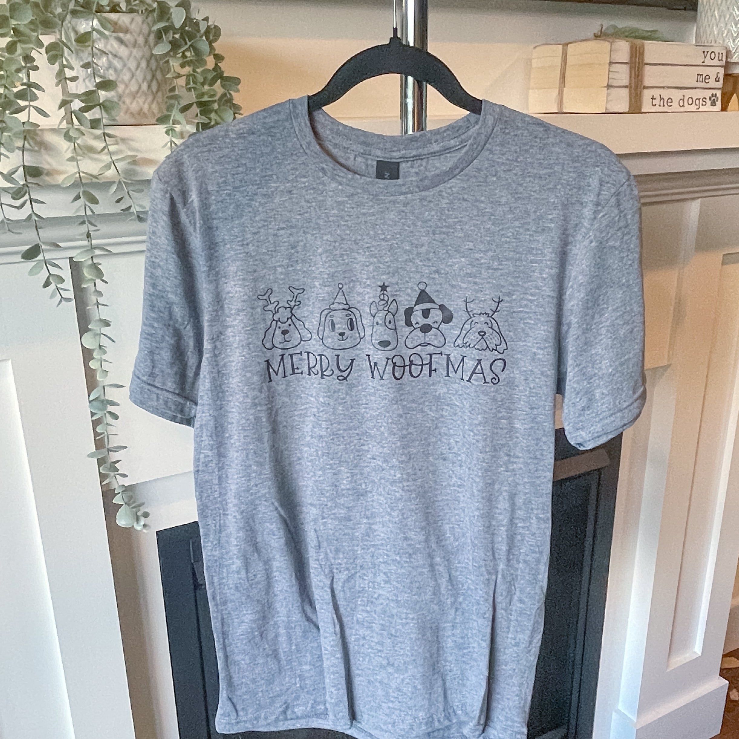 Gray t-shirt with text on a hanger in a room with a fireplace and plants.