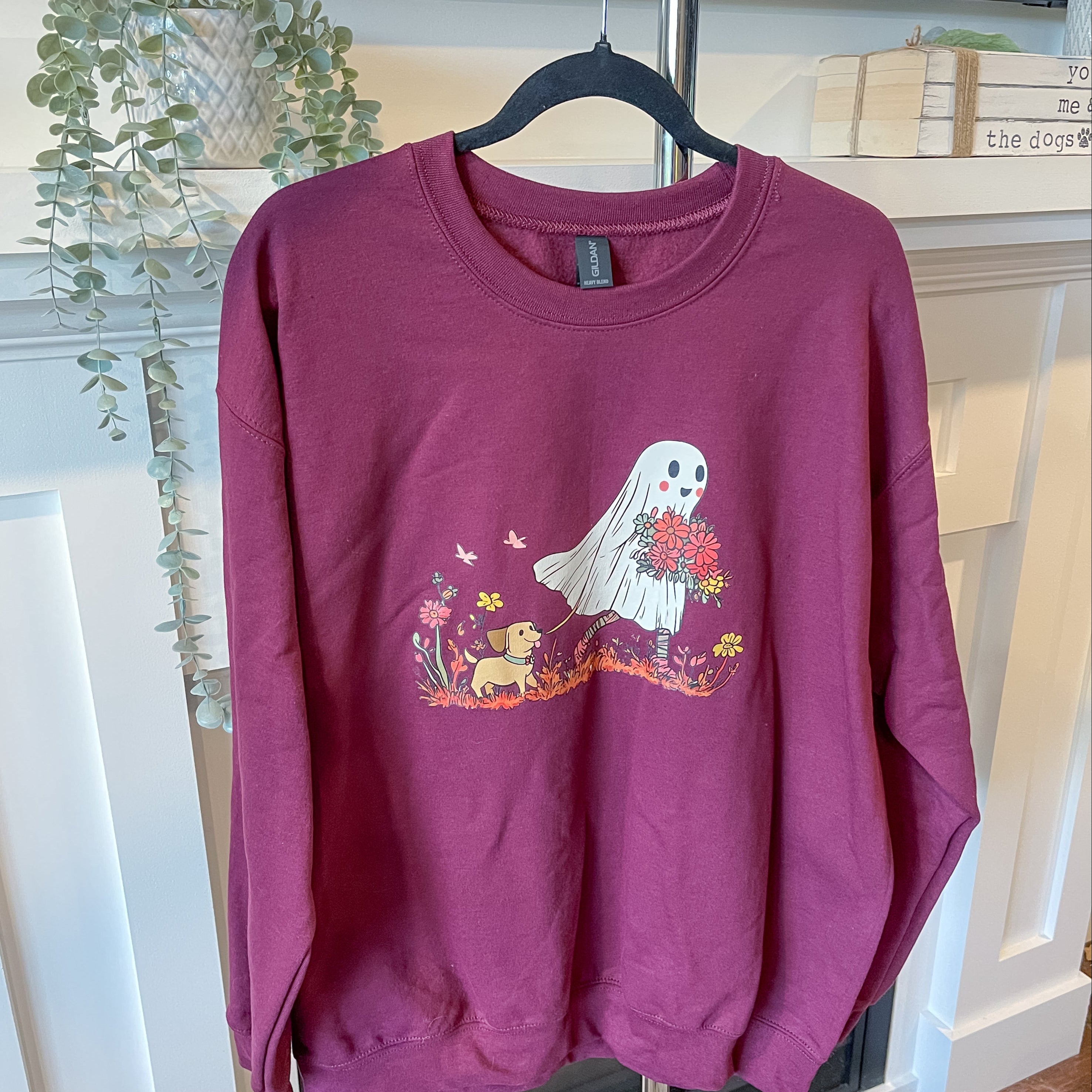 Maroon sweatshirt with a ghost and dog design on a hanger.