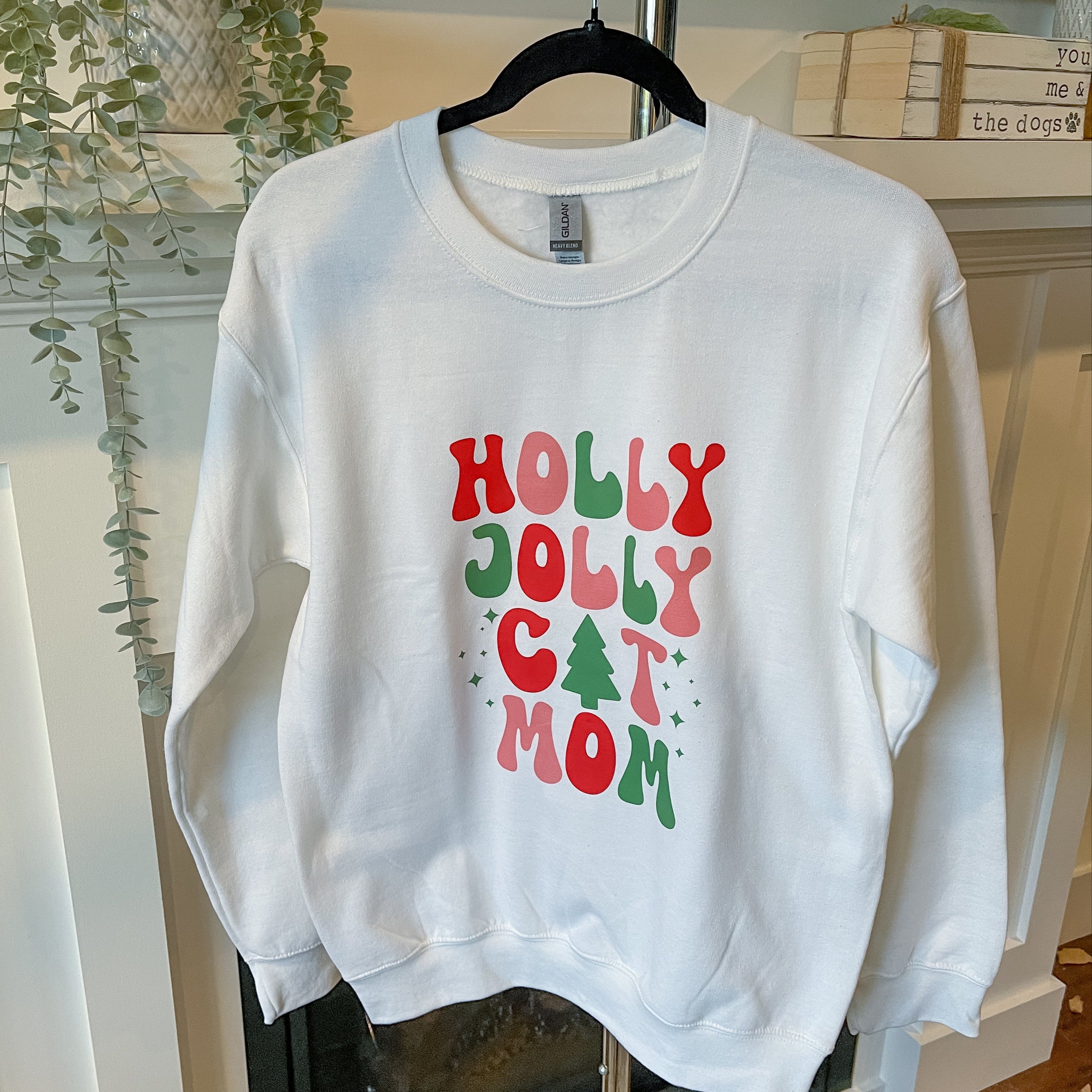 White sweatshirt with 'Holly Jolly Cat Mom' text on a hanger.